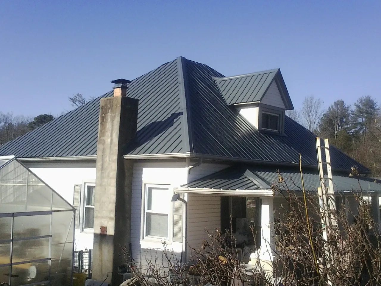 Dark blue standing seam metal roof on a white farmhouse with dormer — Slate & Tile Roof Repair by Roofing Brothers in Lehigh Acres