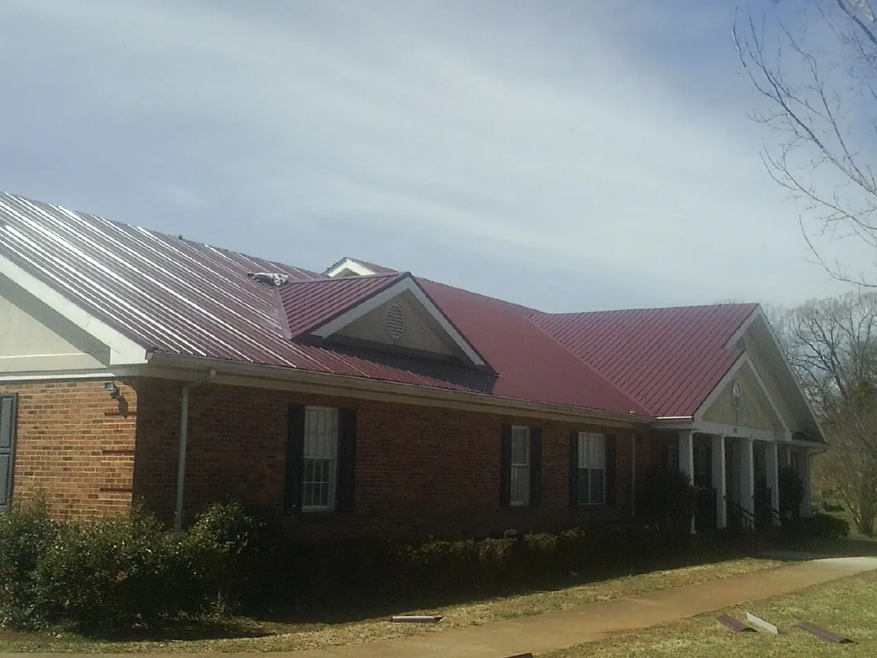 Red metal roof with gabled entries on a long brick building, from a Hail Damage Roof Repair job in Lehigh Acres