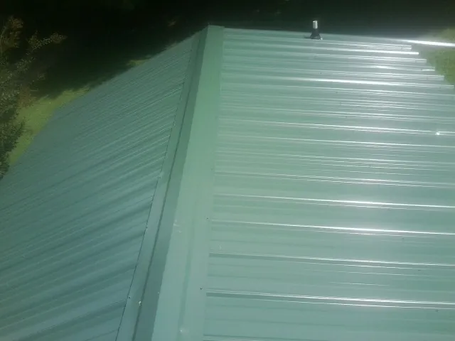 New green metal panels meeting at the ridge of a roof — Flat Roof Repair work by our crew in Lehigh Acres