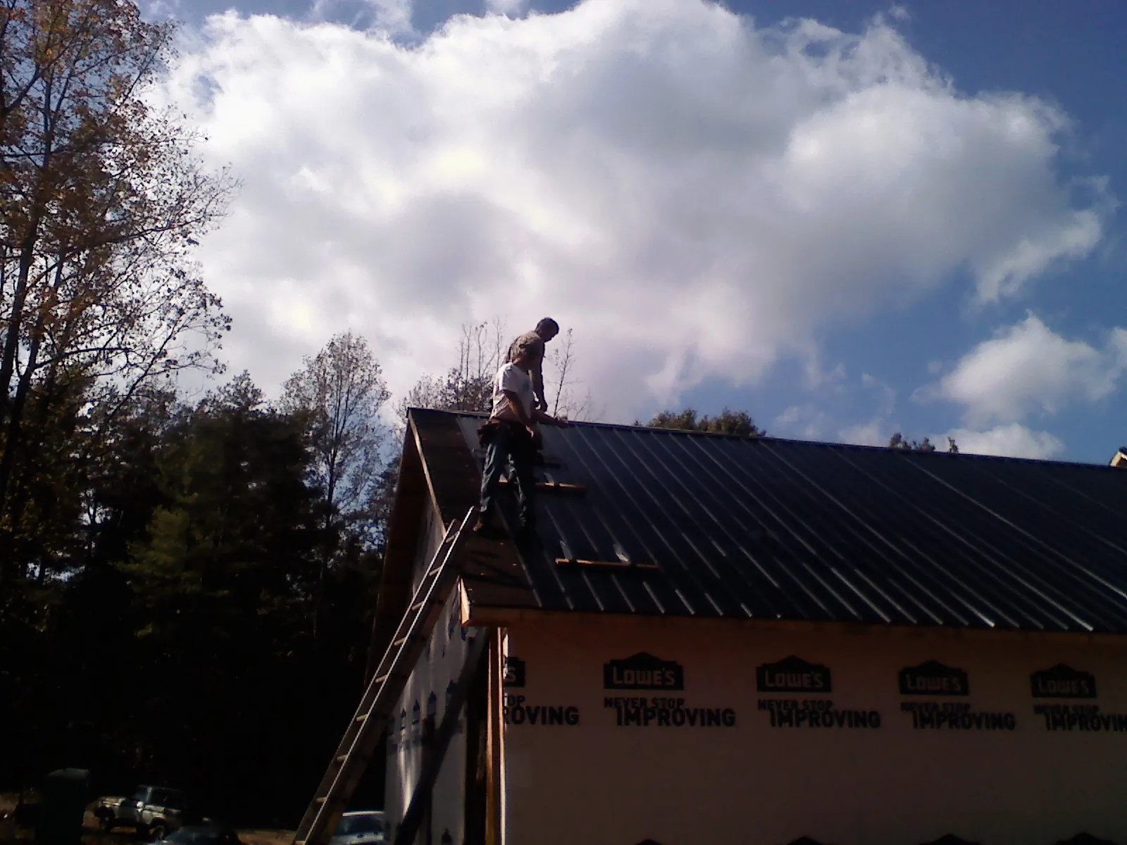Roofer fastening dark metal panels high against a cloudy sky, from a Roof Inspection job in Lehigh Acres