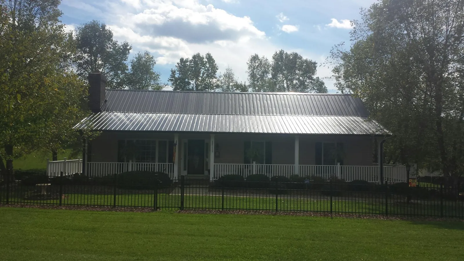 Gray metal roof on a brick ranch with a full width front porch — Gutter Guard Installation work by our crew in Lehigh Acres