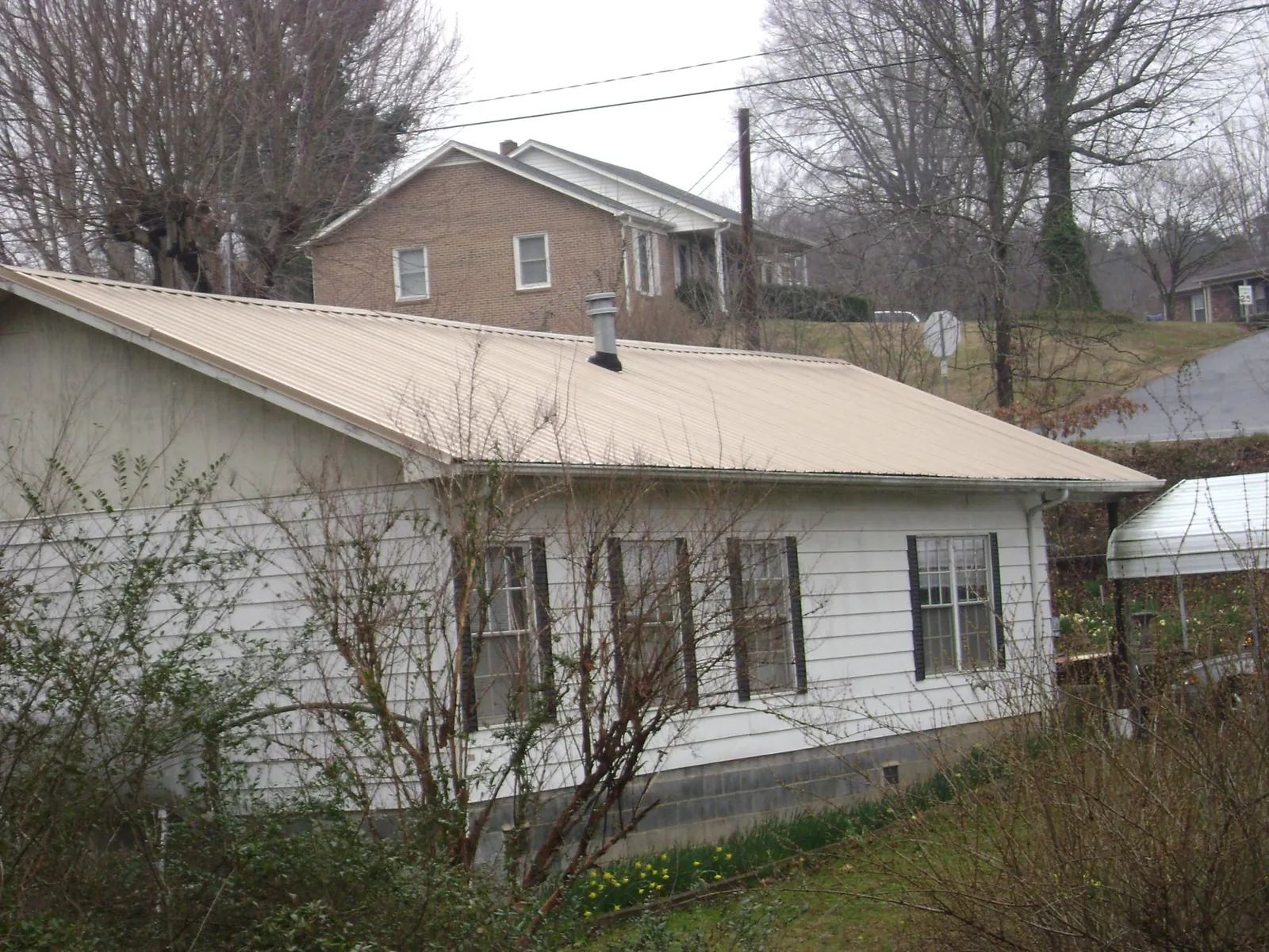 Tan metal roof on a white sided house set into a hillside — Commercial Roofing by Roofing Brothers in Lehigh Acres