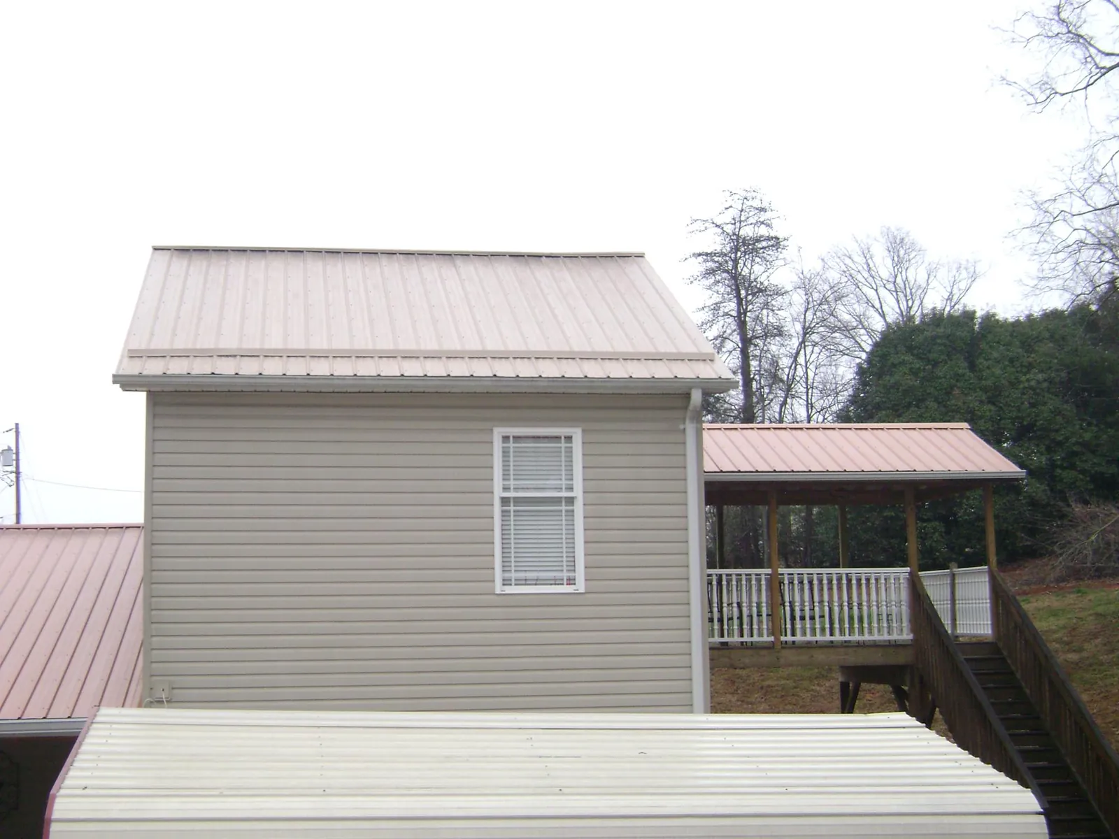 Tan metal roofs on a two story addition and attached porch, from a Roof Replacement job in Lehigh Acres